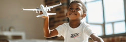 African American boy plays with a toy plane. Wears a white t-shirt with the Xreme Riderz logo on it. 